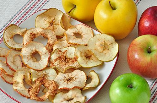 baked apple chips on a plate surrounded by whole apples