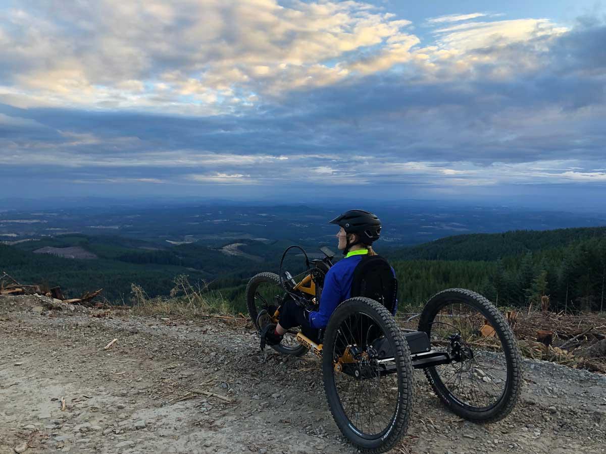 Lizzy sitting in a mountain bike that has 3 tires overlooking a green valley