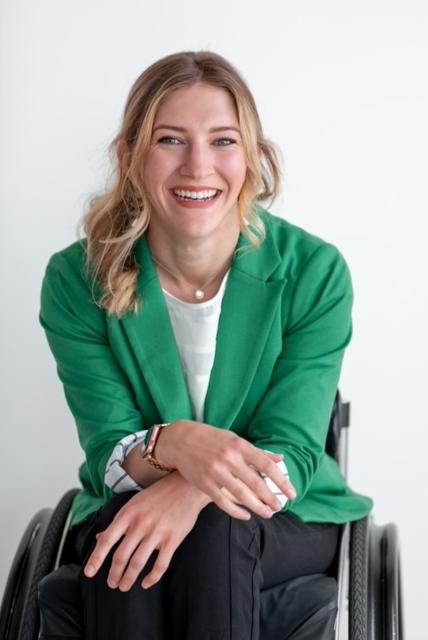Lizzy Ragan in a green blazer and black pants sitting in a wheelchair